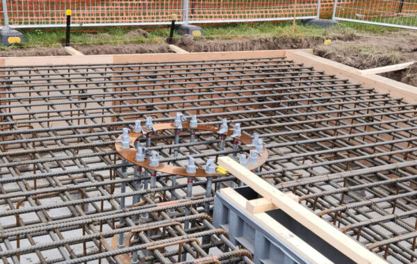 Dense steel rebar grid for a concrete slab being prepared, with formwork and circular anchor rings visible on a construction site.