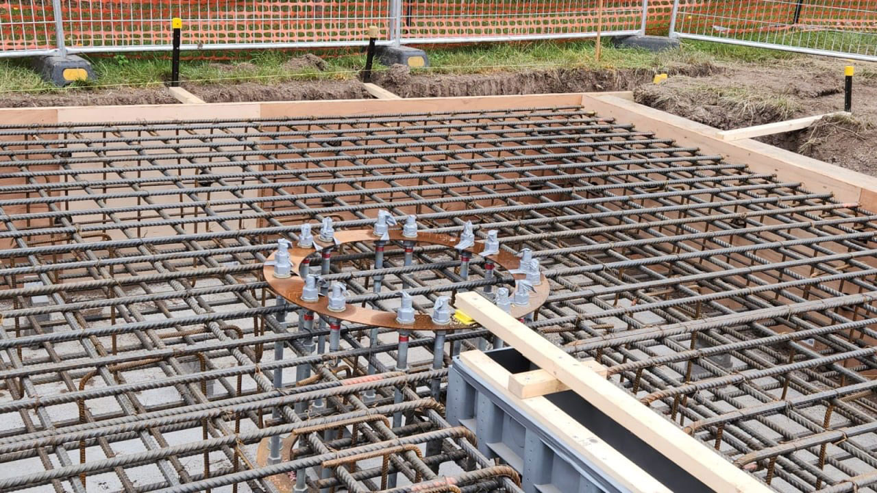 Dense steel rebar grid for a concrete slab being prepared, with formwork and circular anchor rings visible on a construction site.