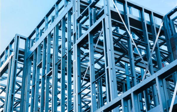 Steel building frame under construction with vertical and horizontal metal beams against a blue sky.